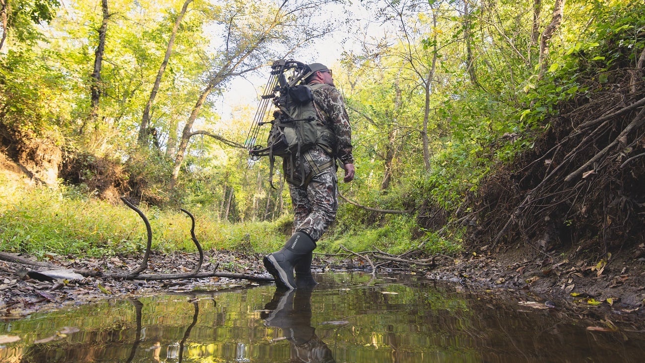 A hunter walks in a creek through the woods to help minimize his scent trail